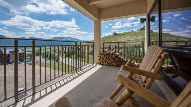 A balcony with a view of a lake and mountains, wooden chairs, and a stack of firewood. - Lovely Modern Plaza Condo - No Cleaning Fee! by RedAwning (Crested Butte)