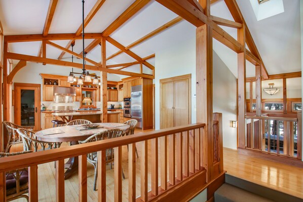 A spacious kitchen with wooden beams, a dining area with wicker chairs, and a view through a glass door. - Beautiful Craftsman Style Lake Home (Hayward)