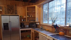 Een compacte keuken met houten kastjes, een roestvrijstalen koelkast, een magnetron, een vaatwasser en een fornuis.
