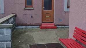 Ein rosafarbenes Gebäude mit einer Holztür, zwei Fenstern und einer roten Bank vor der Fassade.