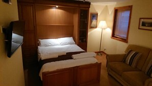 Ein Hotelzimmer mit einem Holzbett, einem Nachttisch mit Lampe, einer Couch und einem Spiegel an der Wand.