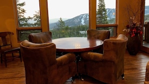 A room with a round wooden table and four leather chairs, large windows with a mountain view, and a vase with red flowers on the right. - Moonlight Magic!  Best Views In Big Sky!  True Ski-In/Ski-Out!  Heated Ski Room! (Big Sky)