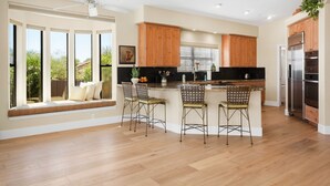 Une cuisine moderne avec des meubles en bois, un grand îlot central doté de tabourets, et une vue sur l’extérieur.