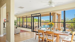 Un vaste espace dédié à la salle à manger, avec une grande table et des chaises, une vue sur une piscine et un ventilateur de plafond.