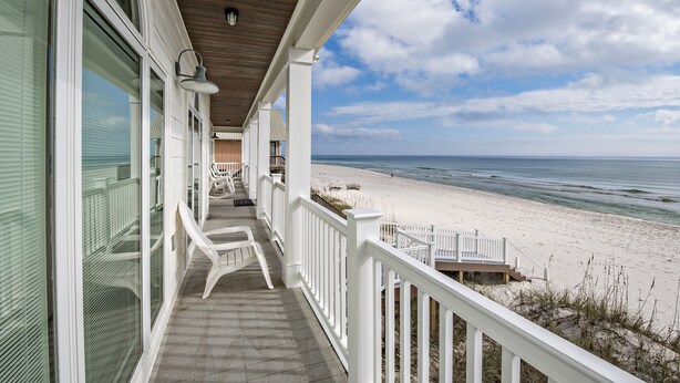 Ein strandnahes Anwesen mit überdachter Veranda, weißen Geländern und Blick auf den Ozean.