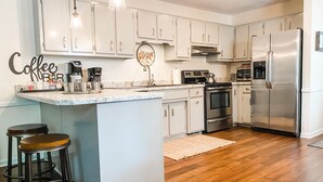A modern kitchen with white cabinets, a stainless steel refrigerator, a coffee bar, and two stools. - Luxurious 2BR /2Bath with Outdoor Courtyard and Garage in Downtown Bardstown (Bardstown)
