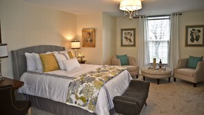 A hotel room with a large bed, two armchairs, a small ottoman, a nightstand with a lamp, and framed botanical prints on the walls. - Luxurious 2BR /2Bath with Outdoor Courtyard and Garage in Downtown Bardstown (Bardstown)