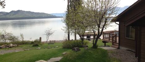 A lakeside cabin with a deck, a grassy yard, and a stone pathway leading to the dock.