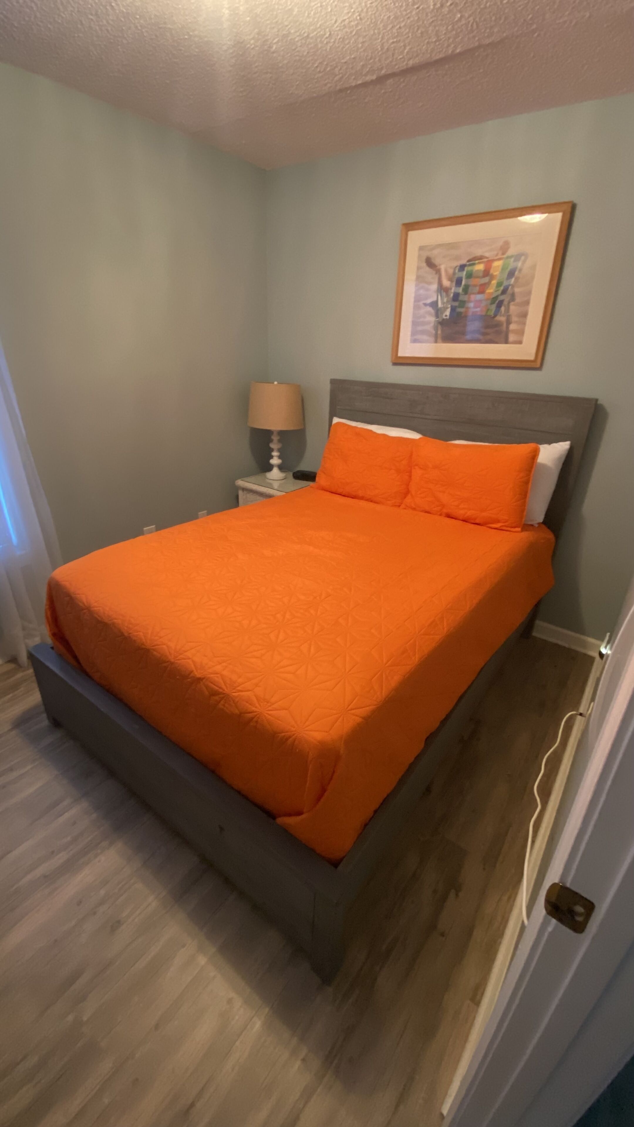 Ein Schlafzimmer mit einem Bett, einem Nachttisch, einer Lampe und einem gerahmten Bild an der Wand.