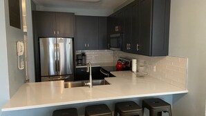 A modern kitchen with dark cabinets, a stainless steel refrigerator, a black stove, and a white countertop. - Oceanview at Surfside-Where the Fun is up and Stress is Down! (Myrtle Beach)