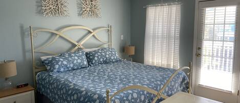 A bedroom with a bed, bedside tables, a nightstand, a lamp, decorative wall art, and a window with blinds.