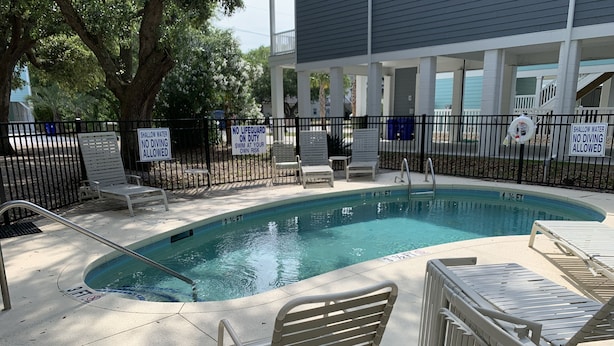 A swimming pool with safety signs, lounge chairs, and a covered area with a railing. - Oceanview at Surfside-Where the Fun is up and Stress is Down! (Myrtle Beach)