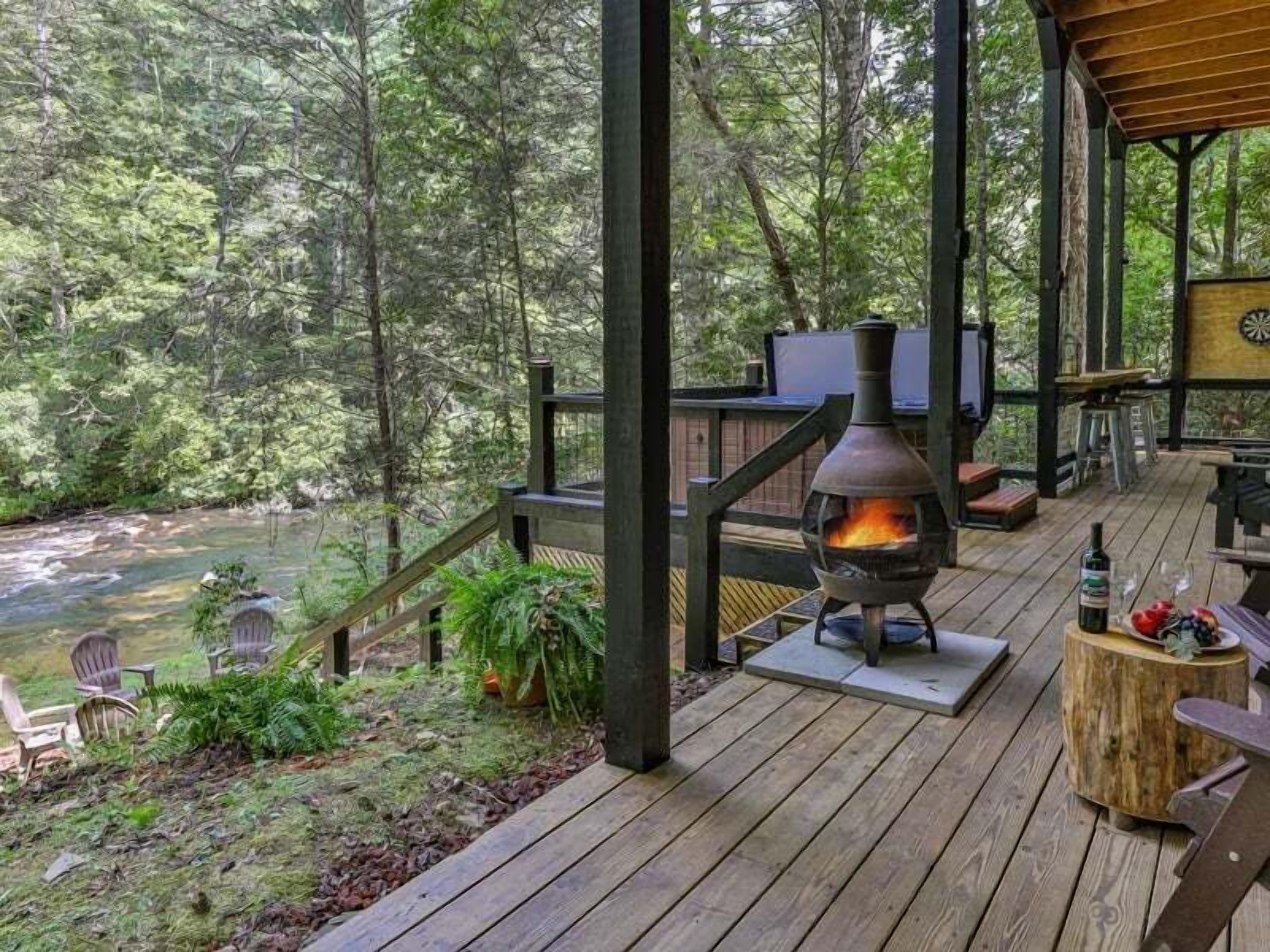 Une terrasse en bois avec un poêle à bois, des sièges d’extérieur et une vue sur une rivière.