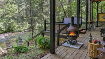 A wooden deck with a wood-burning stove, outdoor seating, and a view of a river.