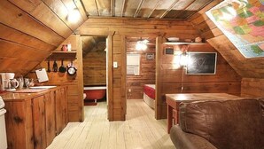 Acogedor cuarto ático con paredes de madera y techo inclinado. Cuenta con una kitchenette con pileta y estufa, una mesa de comedor y un sofá.