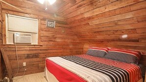 Un dormitorio de cabaña de madera con una cama, una ventana con persianas y una pequeña foto en la pared.