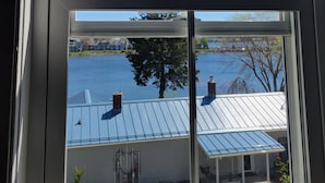 Una ventana con vista a una casa de techo azul, cerca de una valla blanca y un árbol.