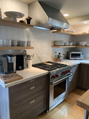A modern kitchen with a built-in stove, oven, and microwave. There are wooden shelves with cups and plates, and a coffee maker on the counter. - Sonoma Valley-Beautiful Glen Ellen Wine Country Retreat - Amenities Galore! (Glen Ellen)