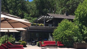 A pool area with red lounge chairs, a covered seating area, and a building with a tiled roof. - Sonoma Valley-Beautiful Glen Ellen Wine Country Retreat - Amenities Galore! (Glen Ellen)
