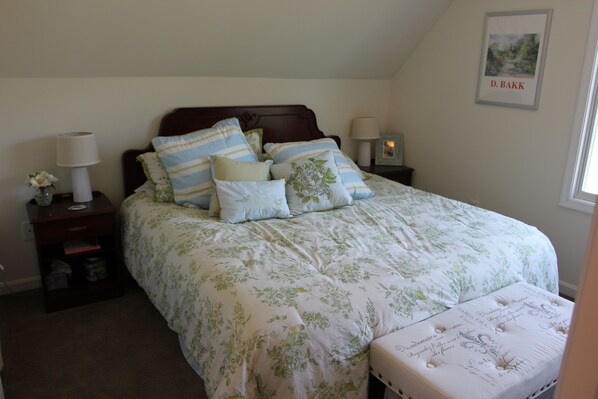 A neatly made bed with floral bedding, a bedside table with a lamp, and a framed picture on the wall.