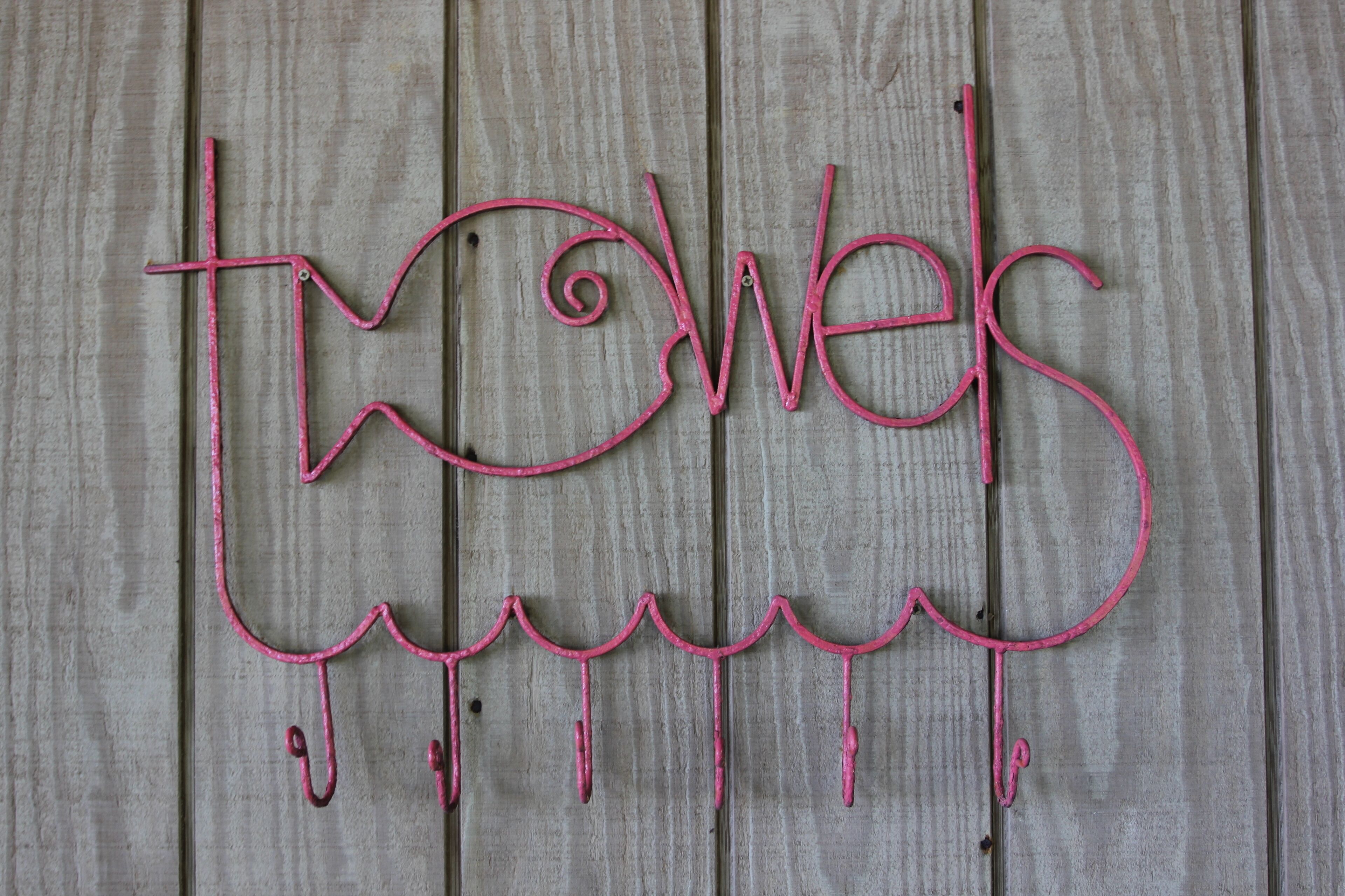 A pink metal sign with the word "towels" on a wooden background.