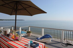 A deck with a striped tablecloth, a blue basket, and a beige umbrella.