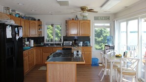 A kitchen with wooden cabinets, a black refrigerator, a stove, and a dining area with white chairs. - Beach Cottage With A Spectacular View ~ Your Own Private Beach ~ Includes Kayaks (Ridge)