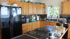 A kitchen with wooden cabinets, a black refrigerator, a stove, and various kitchen appliances. - Beach Cottage With A Spectacular View ~ Your Own Private Beach ~ Includes Kayaks (Ridge)