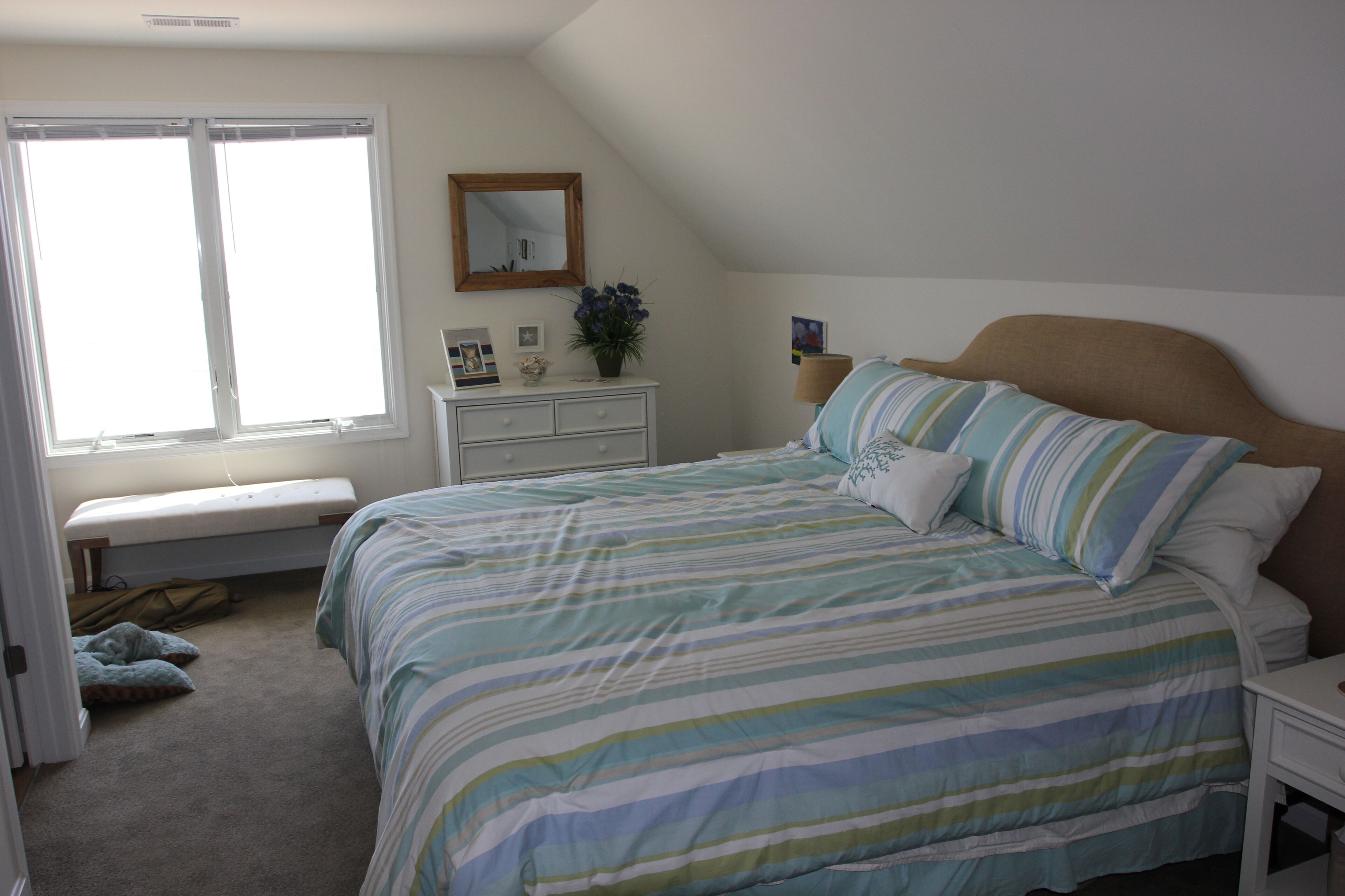 A bedroom with a bed, a bench, a dresser, and a window.