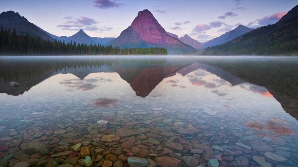A calm lake with clear reflections of mountains and trees, surrounded by a forest. - Rising Wolf: Spacius 2-bedroom, 2-bathroom with Amazing Mountain Views (East Glacier Park)