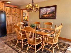A dining area with wooden chairs and a table, a chandelier, and a framed picture on the wall. - Rising Wolf: Spacius 2-bedroom, 2-bathroom with Amazing Mountain Views (East Glacier Park)