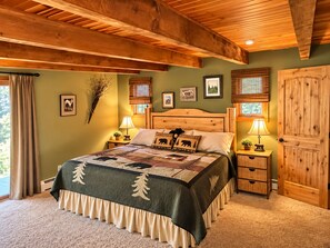A bedroom with a large bed, wooden headboard, two bedside tables with lamps, a wooden wardrobe, and framed pictures on the walls. - Rising Wolf: Spacius 2-bedroom, 2-bathroom with Amazing Mountain Views (East Glacier Park)