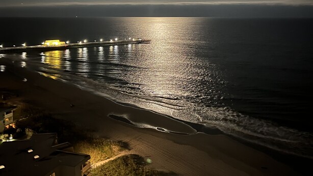 A nighttime beach scene with a pier and buildings in the foreground. - Luxurious Oceanfront Condo Ocean Views throughout in prestigious Maisons-sur-Mer (Myrtle Beach)