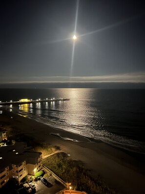 A nighttime beach scene with a pier and buildings in the foreground.