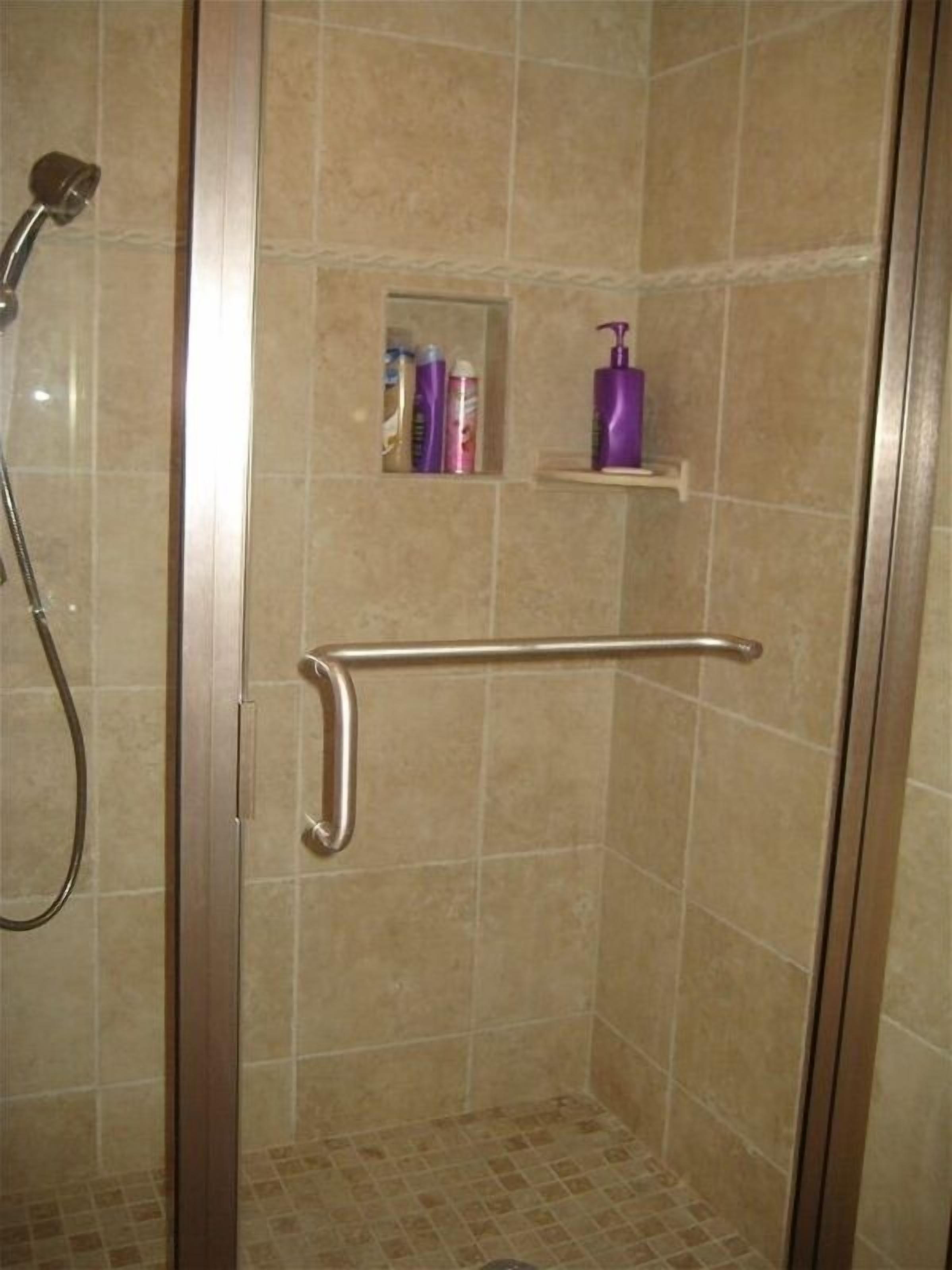 Un espace douche équipé d’une barre d’appui, d’un pommeau de douche et d’une étagère pour les articles de toilette.