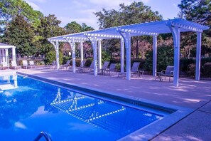 Uma área de piscina com piscina azul cristalina, pérgulas brancas e espreguiçadeiras.