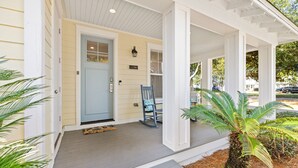 A porch with a blue door, a rocking chair, and a small palm tree. - 1381 Laurel Grove 3 Bedroom Home by RedAwning (Miramar Beach)