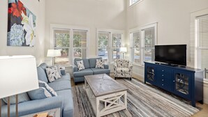A living room with a blue sofa, a coffee table, a TV on a cabinet, and a painting on the wall. - 1381 Laurel Grove 3 Bedroom Home by RedAwning (Miramar Beach)