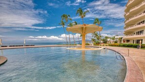 A pool with a central fountain, palm trees, and a beachfront view. - Beachfront 3-bedroom condo with pool (Bahia de Banderas)