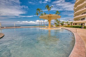 Piscina com uma fonte central, palmeiras e vista para a praia.