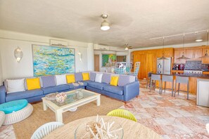 Ein Wohnzimmer mit blauem Sofa, einem Glastisch und einer Küchenzeile mit Holzschränken und einer Bar.