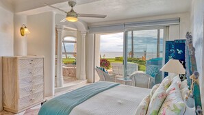 A bedroom with a large bed, a ceiling fan, a view of the ocean, a white wardrobe, and a balcony with outdoor furniture. - Beachfront 3-bedroom condo with pool (Bahia de Banderas)