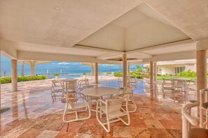 An outdoor patio area with round tables and chairs, a view of the ocean, and a clear sky. - Beachfront 3-bedroom condo with pool (Bahia de Banderas)