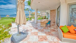 A patio with a beige umbrella, a wooden table, and a sofa with orange cushions. - Beachfront 3-bedroom condo with pool (Bahia de Banderas)