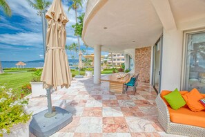 A patio with a beige umbrella, a wooden table, and a sofa with orange cushions. - Beachfront 3-bedroom condo with pool (Bahia de Banderas)