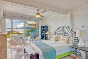 A bedroom with a bed, a ceiling fan, a nightstand, a lamp, and a view of the outdoors. - Beachfront 3-bedroom condo with pool (Bahia de Banderas)