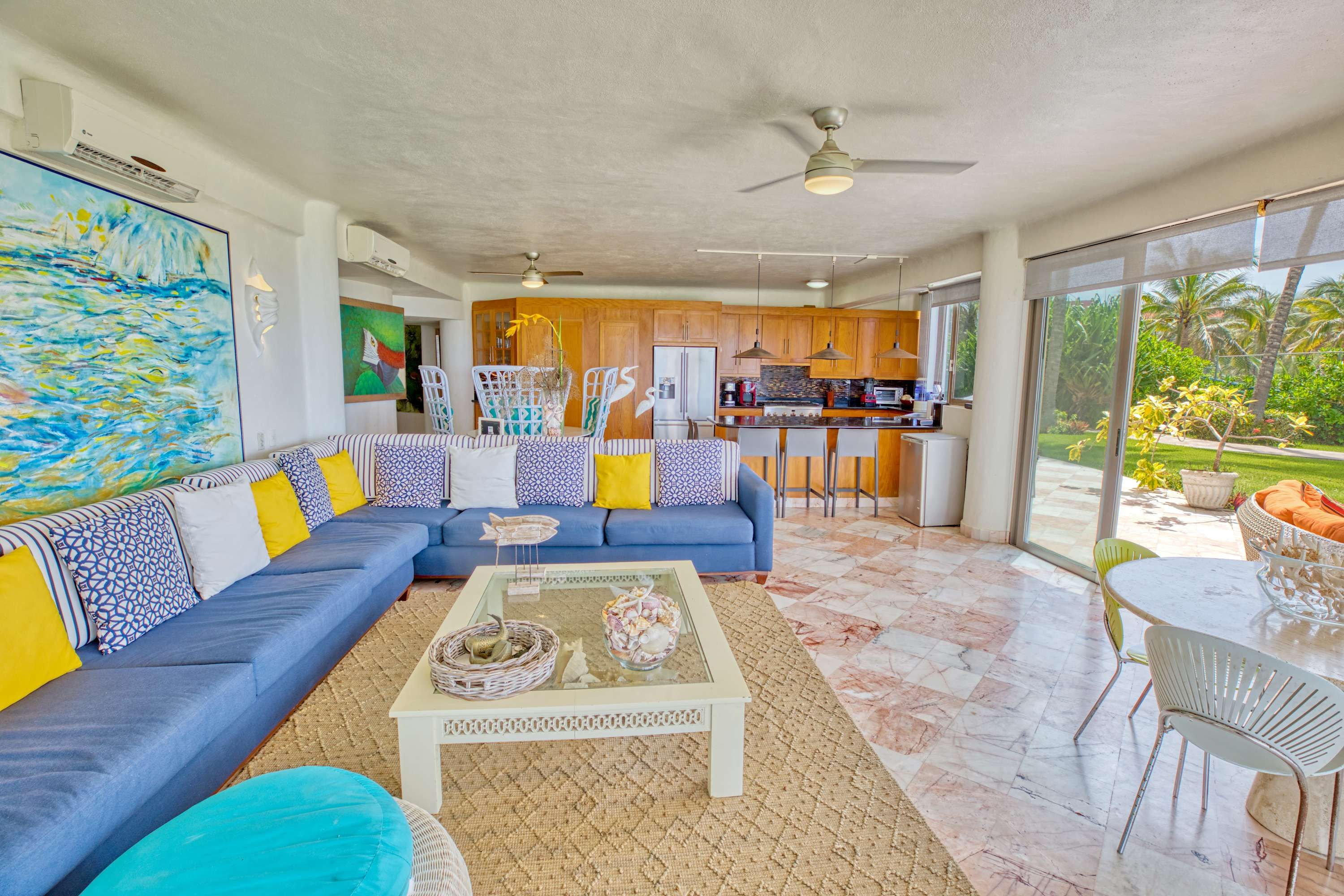 A spacious living room with a blue sofa, a coffee table, and a view of the kitchen and outdoor area.