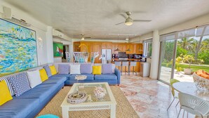 A spacious living room with a blue sofa, a coffee table, and a view of the kitchen and outdoor area. - Beachfront 3-bedroom condo with pool (Bahia de Banderas)