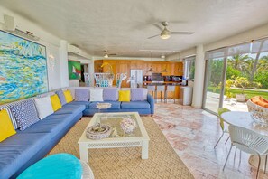 Uma sala de estar espaçosa com um sofá azul, uma mesa de centro e vista para a cozinha e área externa.