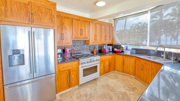 A kitchen with wooden cabinets, stainless steel appliances, and a large window. - Beachfront 3-bedroom condo with pool (Bahia de Banderas)